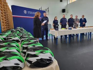 W hali sportowej przy stanowisku z komendą miejską policji we Włocławku odbywa się uroczyste przekazanie rowerowych kasków dla dzieci, w którym uczestniczą funk