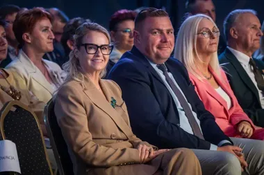 Uczestnicy oficjalnej uroczystości siedzą w rzędach krzeseł w sali konferencyjnej.